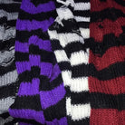 Close-up of three knitted striped sweaters or scarves laid side by side, showing different color combinations: black and purple, black and white, and black and red.