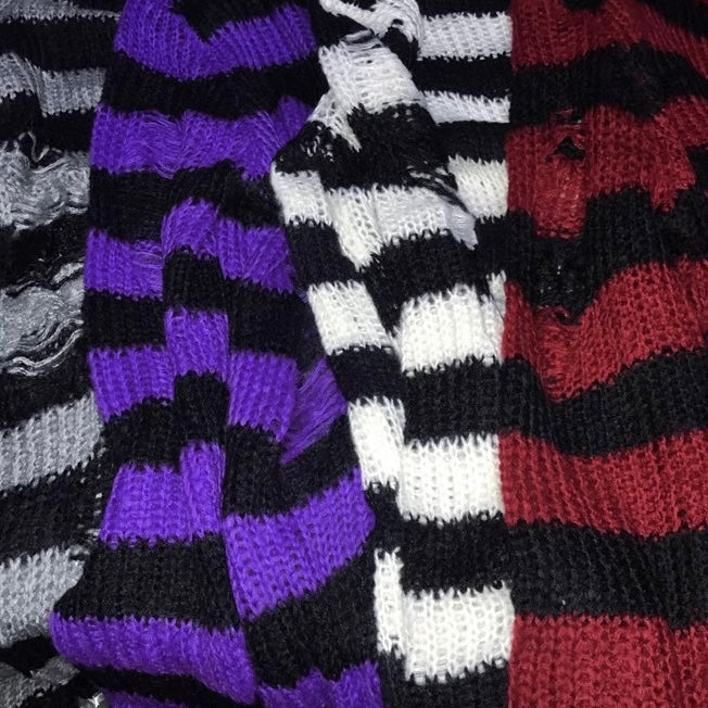 Close-up of three knitted striped sweaters or scarves laid side by side, showing different color combinations: black and purple, black and white, and black and red.