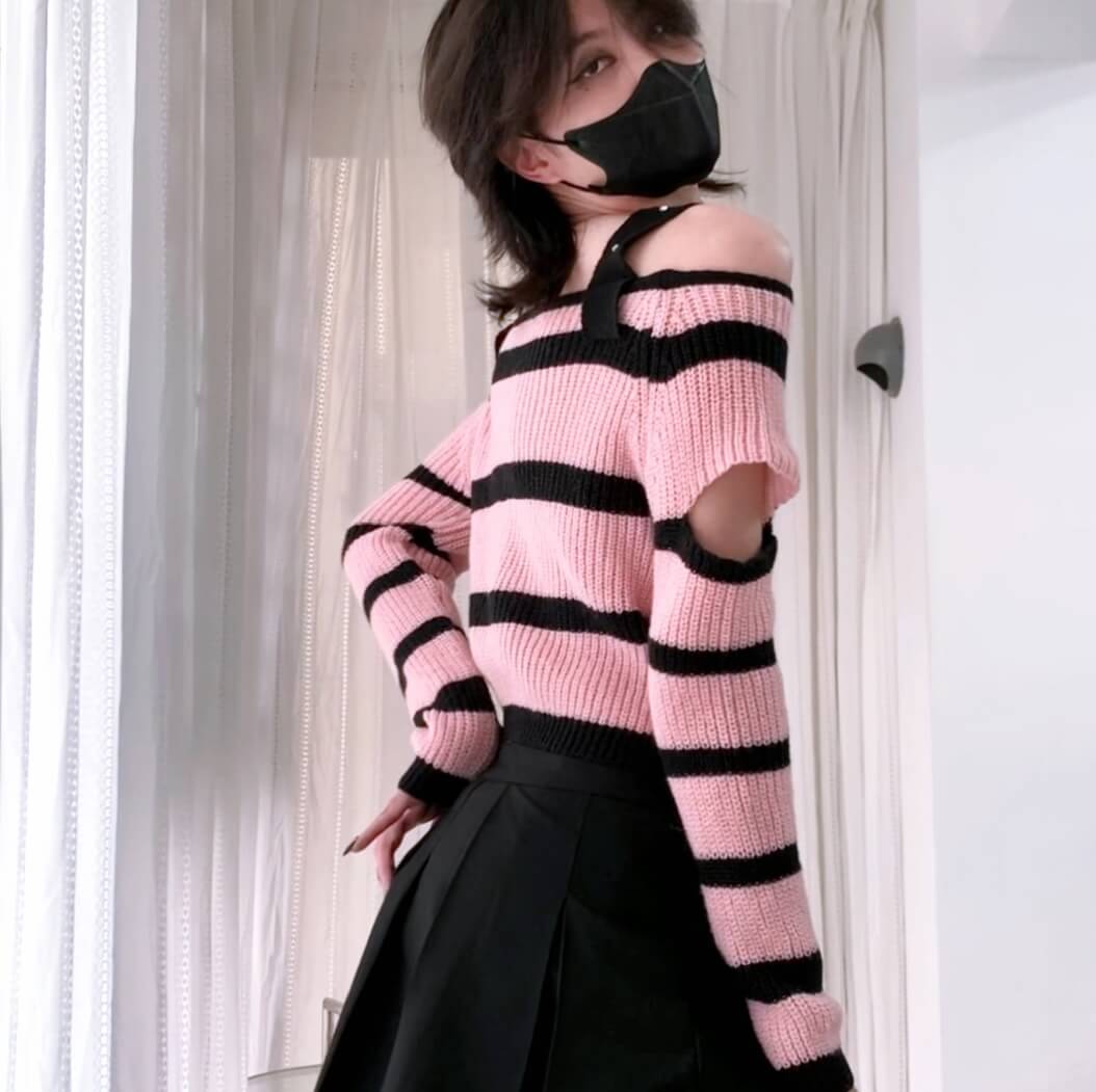 Person wearing a pink and black striped sweater with a black skirt on a plain background