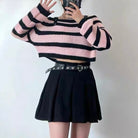 Person wearing a pink and black striped sweater with a black skirt on a plain background