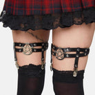 Black leg straps with pentacle design worn over a red plaid skirt and black stockings.