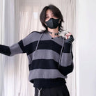 Person wearing a black and gray striped sweater with a plain background