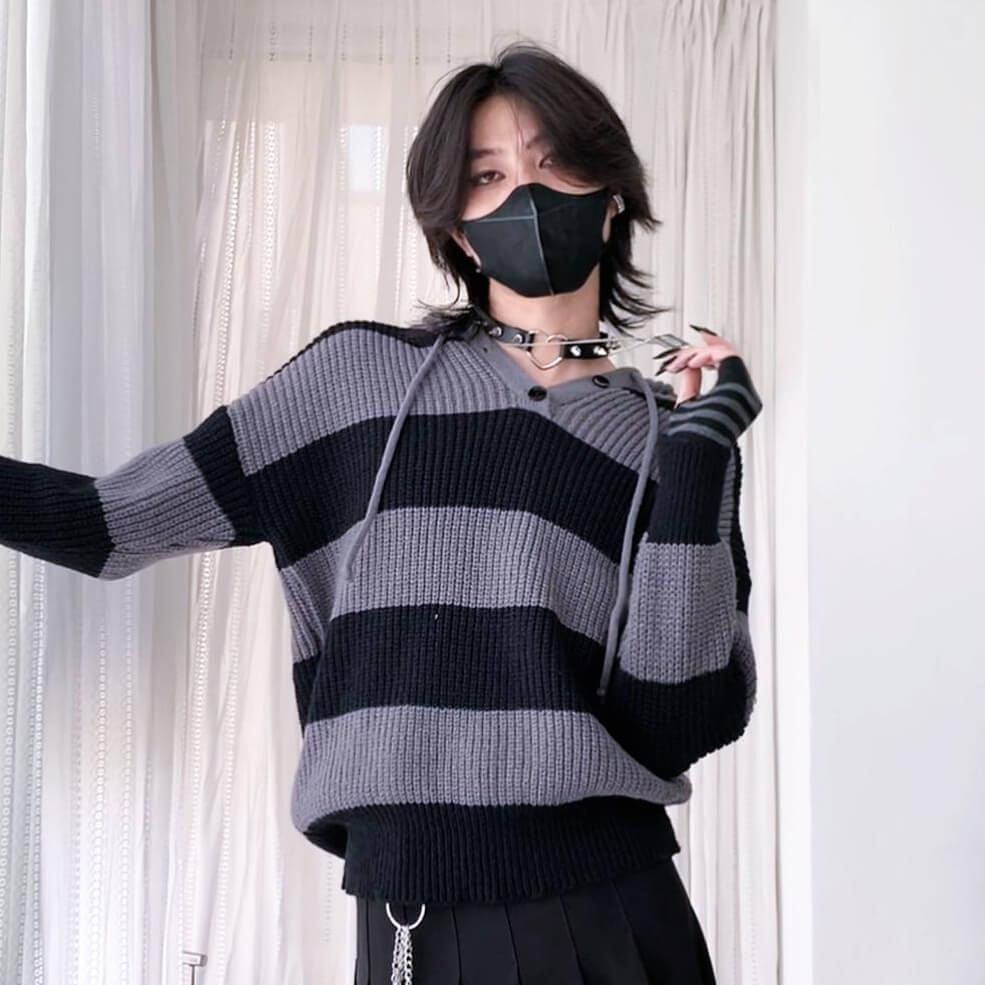 Person wearing a black and gray striped sweater with a plain background