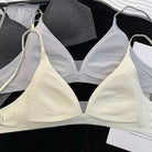 A light cream-colored wireless triangle bra laid flat on a black surface, with other gray and white bras partially visible behind it.