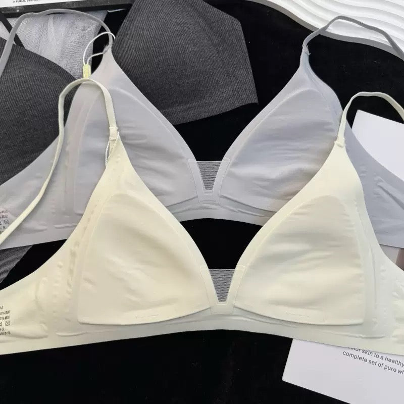 A light cream-colored wireless triangle bra laid flat on a black surface, with other gray and white bras partially visible behind it.