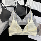 A pale cream-colored wireless triangle bra with adjustable thin straps and a center gore, displayed in front of a gray and white version of the same bra on a black background with styled papers.