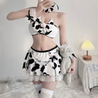 Person wearing a cow print outfit with a skirt and top, holding a plush toy in a room setting.