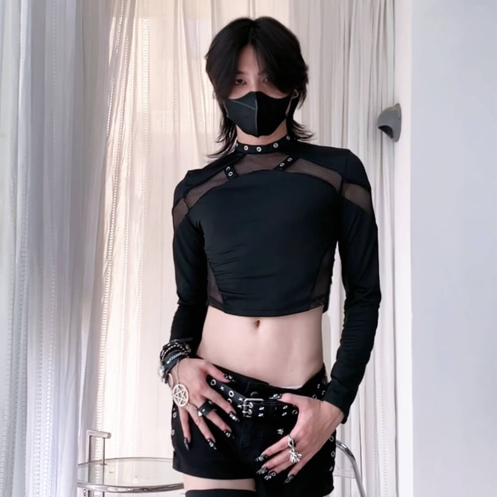 Person wearing a black outfit with sheer panels and a mask indoors.