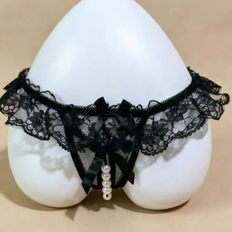 Black lace panties with a ruffled waistband, satin bow, and dangling pearl beads, displayed on a white mannequin against a beige background.