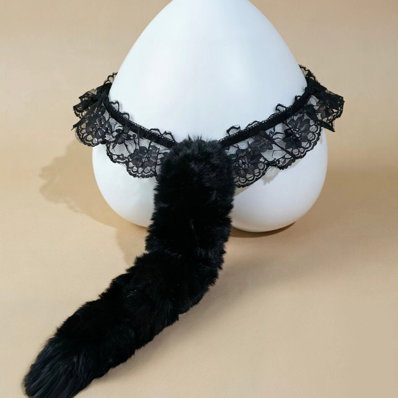 Black faux fur tail accessory with a matching black lace collar, displayed on a white mannequin head against a beige background.
