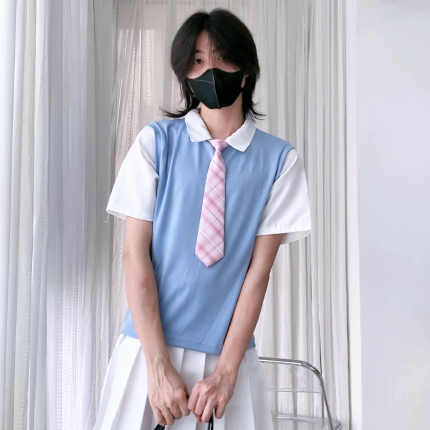 Person wearing a light blue vest over a white shirt with a pink tie, standing against a neutral background.