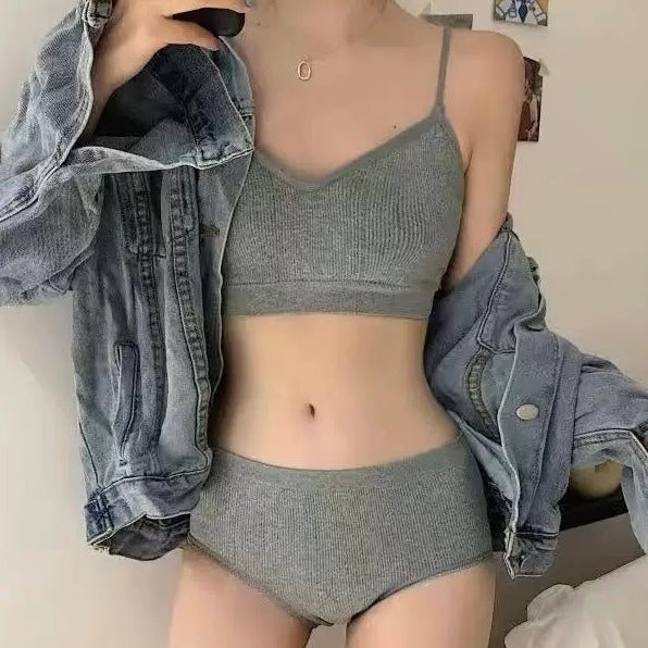 A femboy wearing a ribbed gray two-piece underwear set with a matching bra and high-waisted briefs, styled with an open light-wash denim jacket in a bedroom setting.