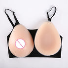 Two beige teardrop-shaped silicone adhesive cup covers displayed on a black bra against a white background, with a pink prohibition symbol over the left cup.