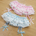 Two pairs of ruffled shorts, one pink and white striped, the other blue and white striped, on a wooden floor.