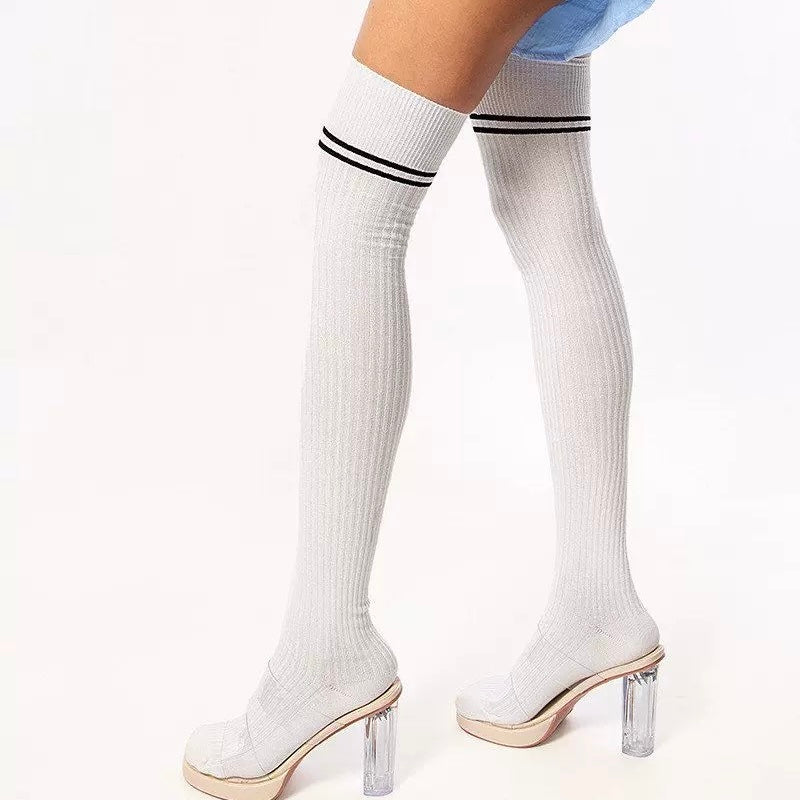 White thigh-high socks with black stripes worn with clear high-heeled shoes on a white background