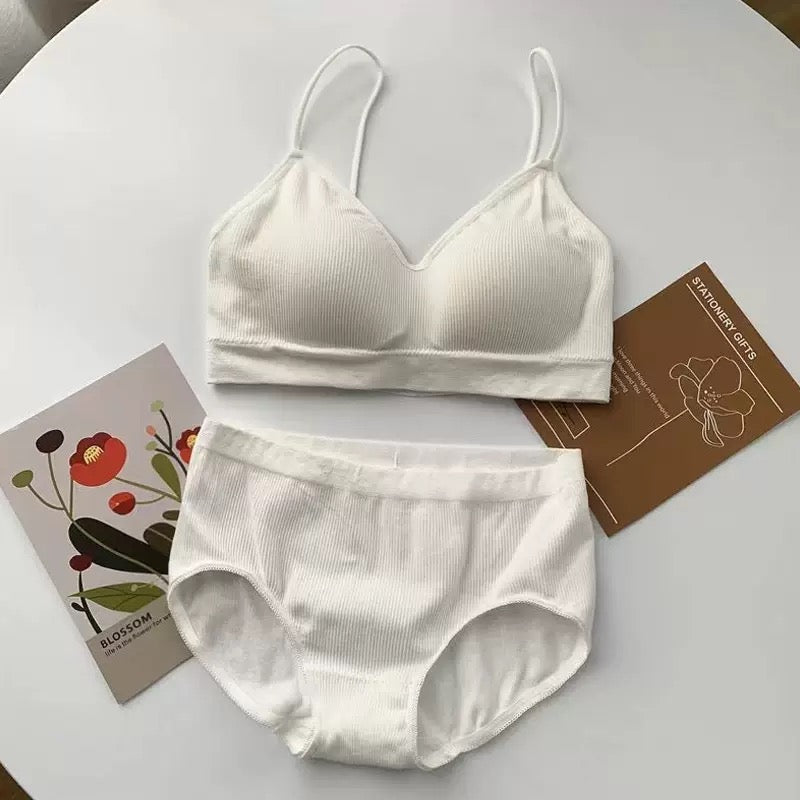 A two-piece white ribbed lingerie set consisting of a bralette and matching briefs, arranged on a white round table with decorative cards.